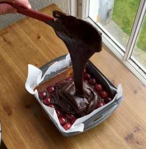 Photo of brownie batter being poured onto cherries and caramel to make Tarte Tatin inspired cherry brownies